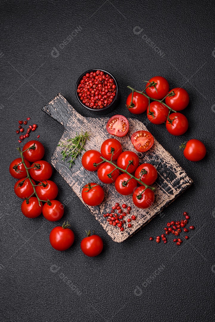 Deliciosos tomates cereja frescos nos galhos como ingrediente para cozinhar um prato vegetariano sobre um fundo escuro de concreto
