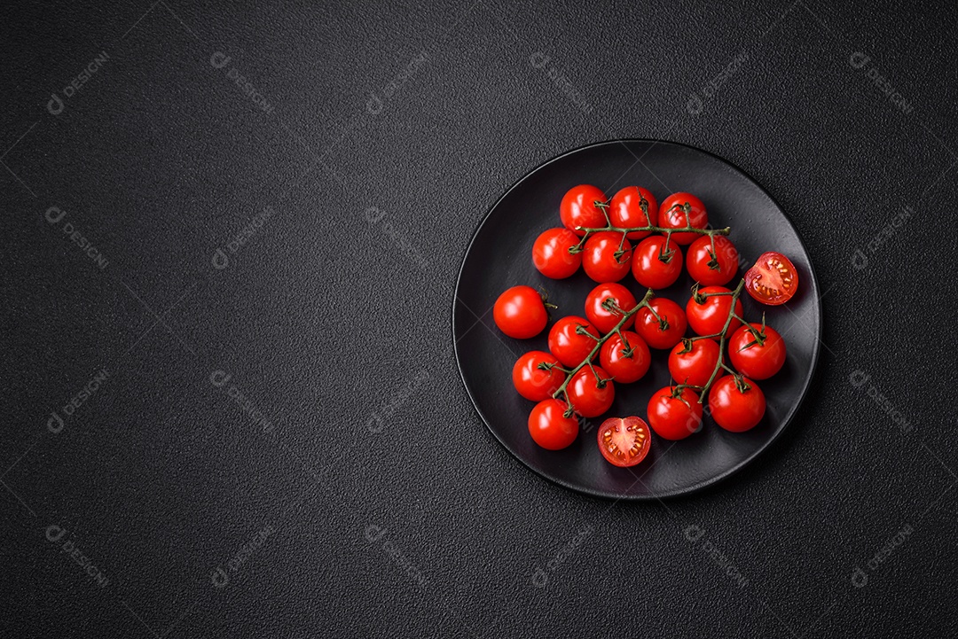 Deliciosos tomates cereja frescos nos galhos como ingrediente para cozinhar um prato vegetariano sobre um fundo escuro de concreto