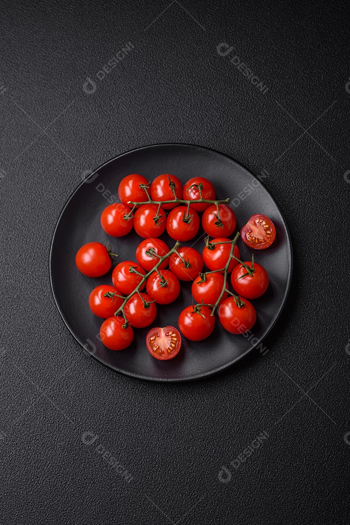 Deliciosos tomates cereja frescos nos galhos como ingrediente para cozinhar um prato vegetariano sobre um fundo escuro de concreto