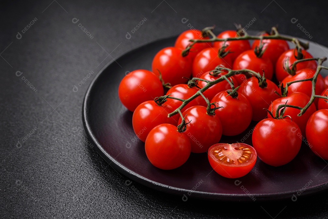 Deliciosos tomates cereja frescos nos galhos como ingrediente para cozinhar um prato vegetariano sobre um fundo escuro de concreto