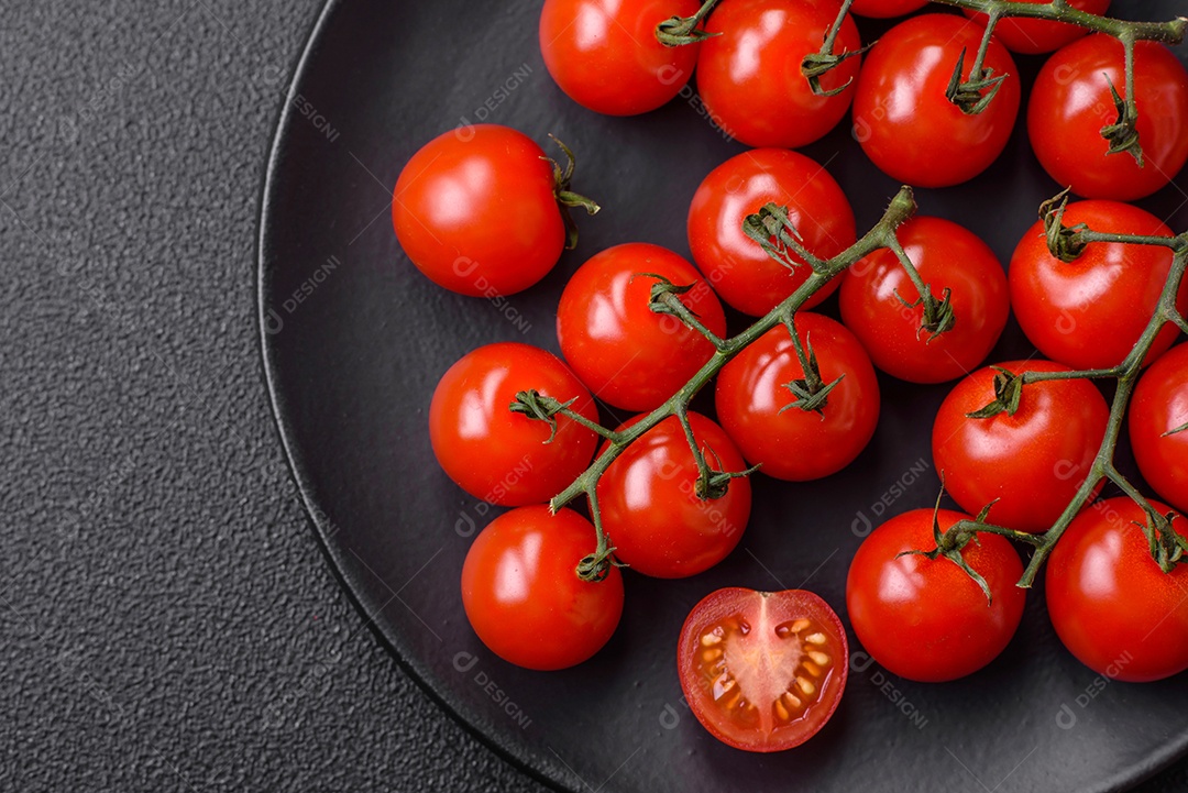 Deliciosos tomates cereja frescos nos galhos como ingrediente para cozinhar um prato vegetariano sobre um fundo escuro de concreto
