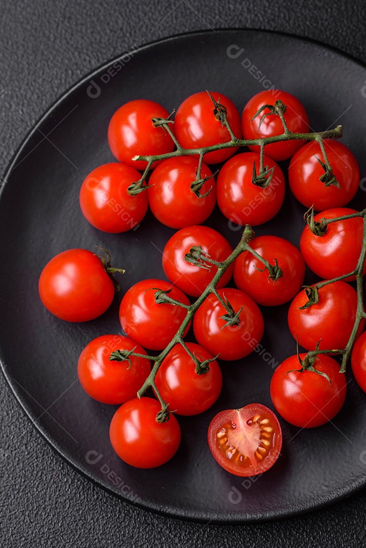 Deliciosos tomates cereja frescos nos galhos como ingrediente para cozinhar um prato vegetariano sobre um fundo escuro de concreto