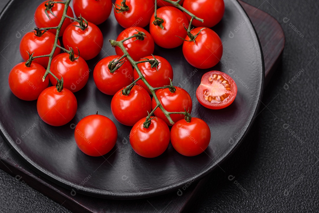 Deliciosos tomates cereja frescos nos galhos como ingrediente para cozinhar um prato vegetariano sobre um fundo escuro de concreto