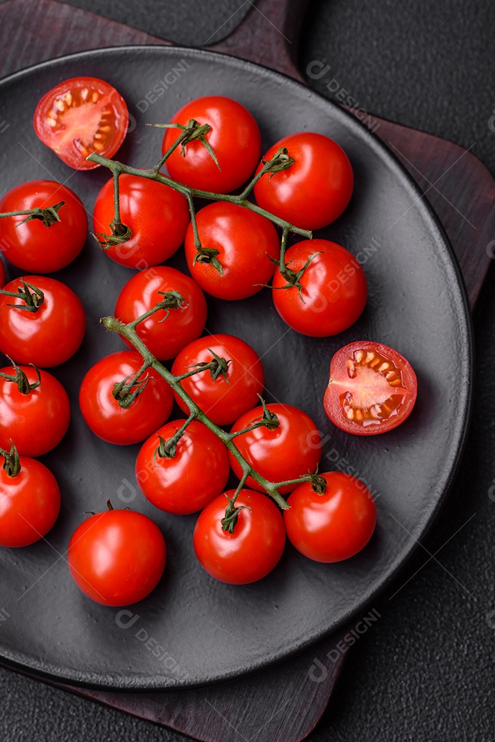 Deliciosos tomates cereja frescos nos galhos como ingrediente para cozinhar um prato vegetariano sobre um fundo escuro de concreto