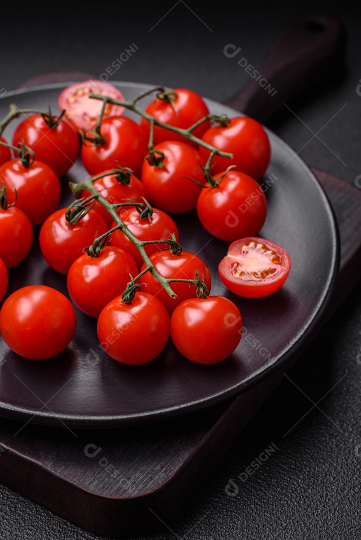Deliciosos tomates cereja frescos nos galhos como ingrediente para cozinhar um prato vegetariano sobre um fundo escuro de concreto