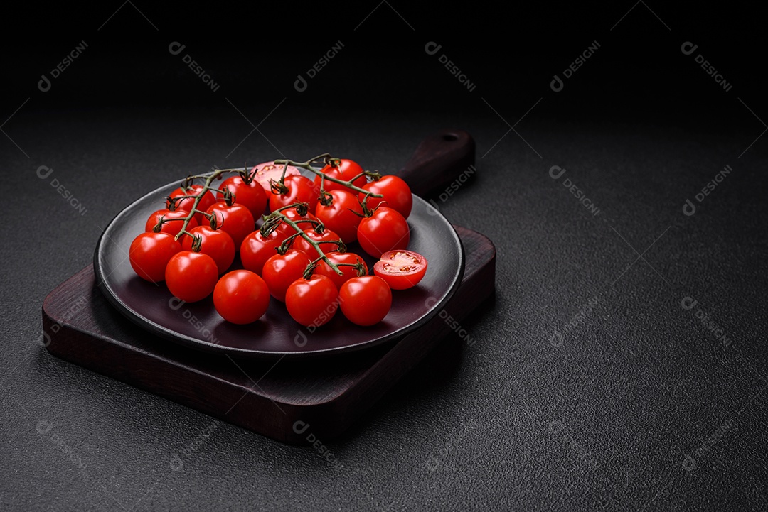 Deliciosos tomates cereja frescos nos galhos como ingrediente para cozinhar um prato vegetariano sobre um fundo escuro de concreto