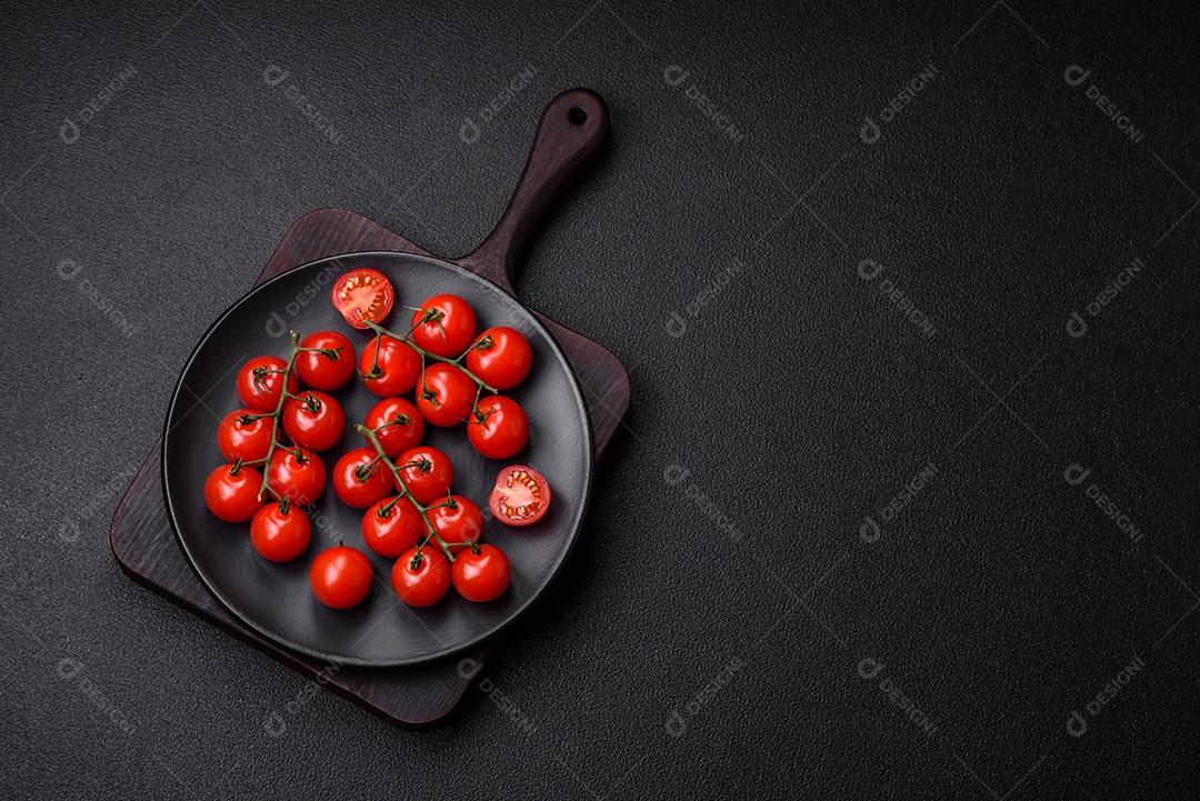 Deliciosos tomates cereja frescos nos galhos como ingrediente para cozinhar um prato vegetariano sobre um fundo escuro de concreto