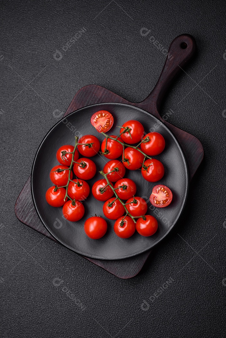 Deliciosos tomates cereja frescos nos galhos como ingrediente para cozinhar um prato vegetariano sobre um fundo escuro de concreto