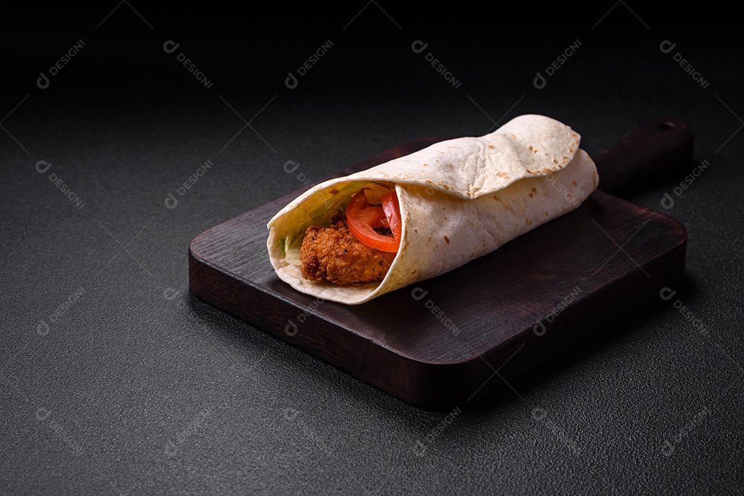 Delicioso rolo com nuggets de frango, tomate, alface e molhos com sal e especiarias sobre fundo escuro de concreto