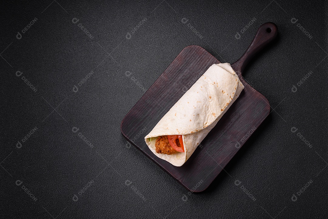 Delicioso rolo com nuggets de frango, tomate, alface e molhos com sal e especiarias sobre fundo escuro de concreto