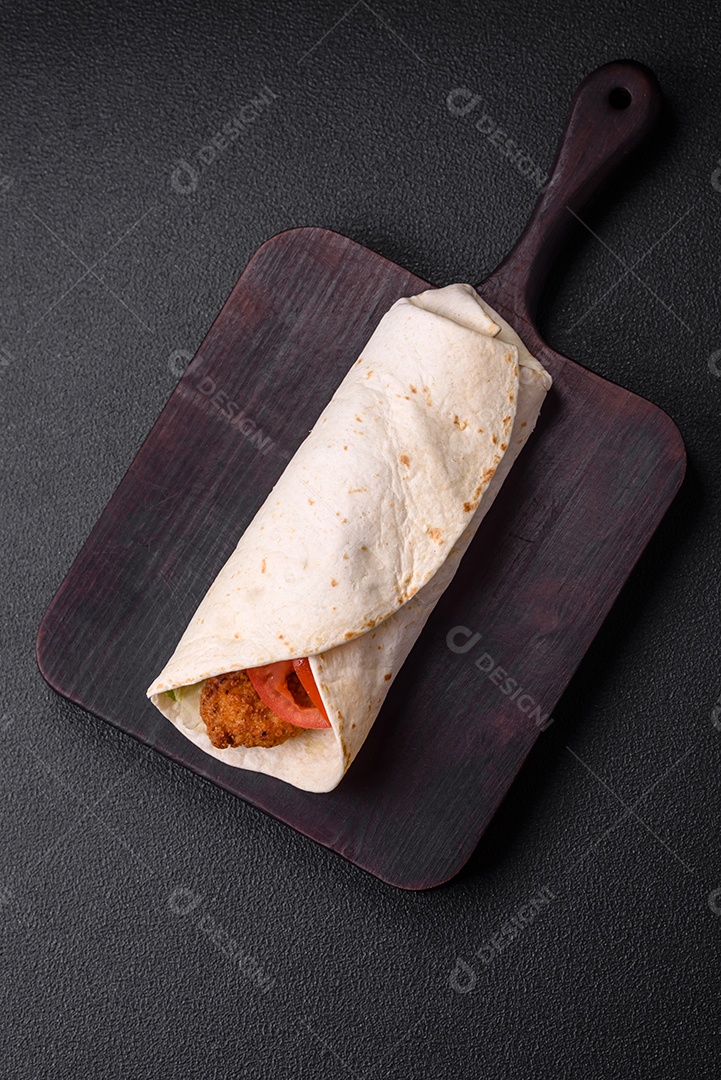 Delicioso rolo com nuggets de frango, tomate, alface e molhos com sal e especiarias sobre fundo escuro de concreto