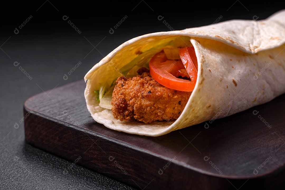 Delicioso rolo com nuggets de frango, tomate, alface e molhos com sal e especiarias sobre fundo escuro de concreto