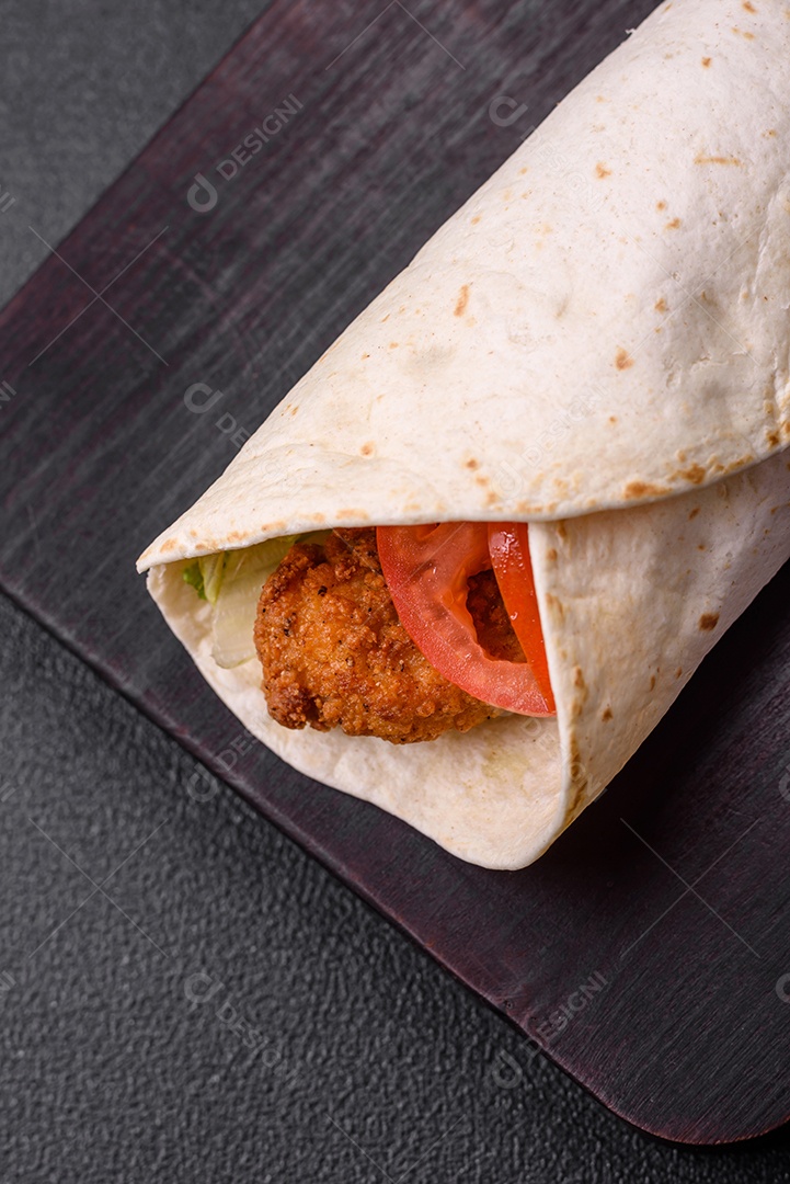 Delicioso rolo com nuggets de frango, tomate, alface e molhos com sal e especiarias sobre fundo escuro de concreto