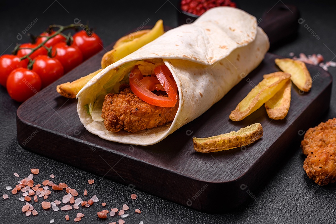 Delicioso rolo com nuggets de frango, tomate, alface e molhos com sal e especiarias sobre fundo escuro de concreto
