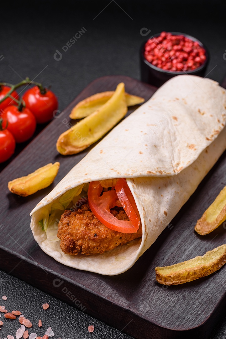 Delicioso rolo com nuggets de frango, tomate, alface e molhos com sal e especiarias sobre fundo escuro de concreto