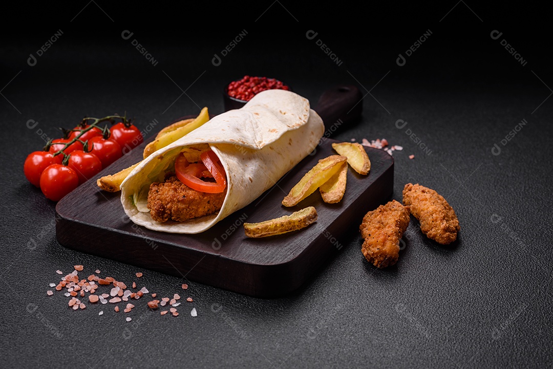 Delicioso rolo com nuggets de frango, tomate, alface e molhos com sal e especiarias sobre fundo escuro de concreto
