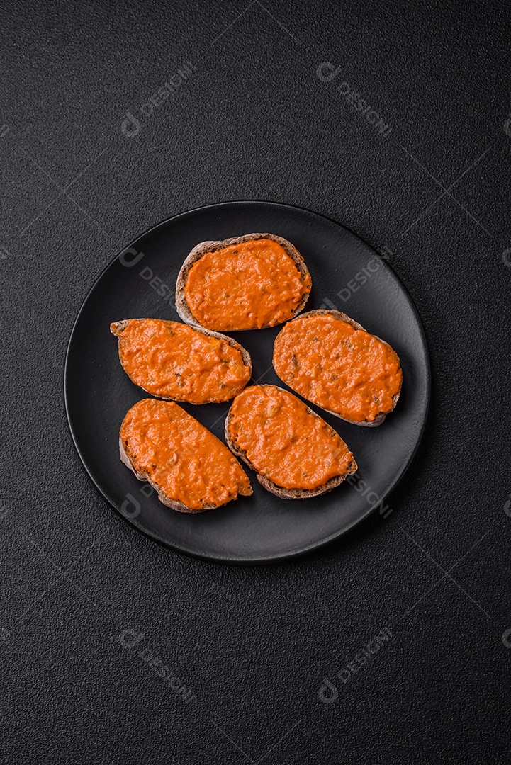 Delicioso sanduíche composto por torradas, molho vermelho com sal, especiarias e ervas sobre um fundo escuro de concreto