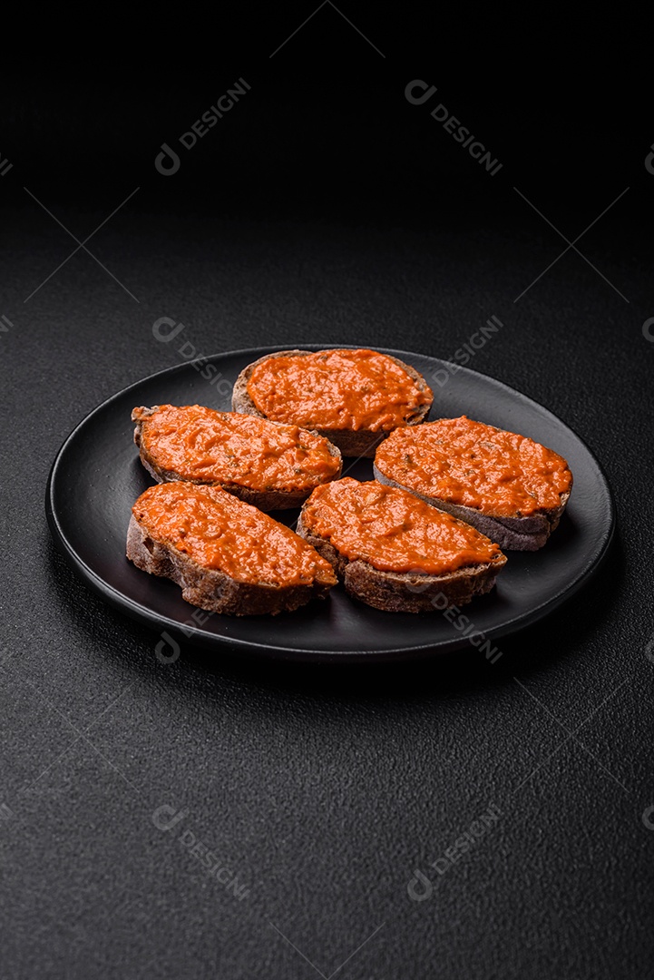 Delicioso sanduíche composto por torradas, molho vermelho com sal, especiarias e ervas sobre um fundo escuro de concreto