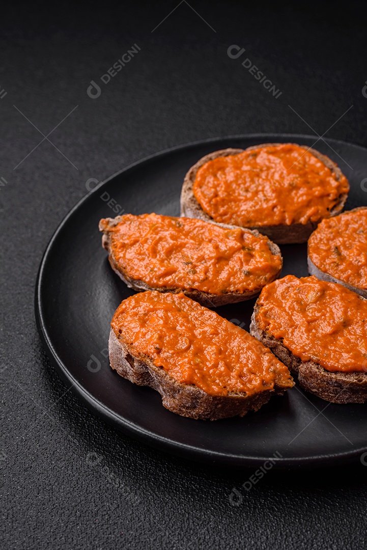 Delicioso sanduíche composto por torradas, molho vermelho com sal, especiarias e ervas sobre um fundo escuro de concreto