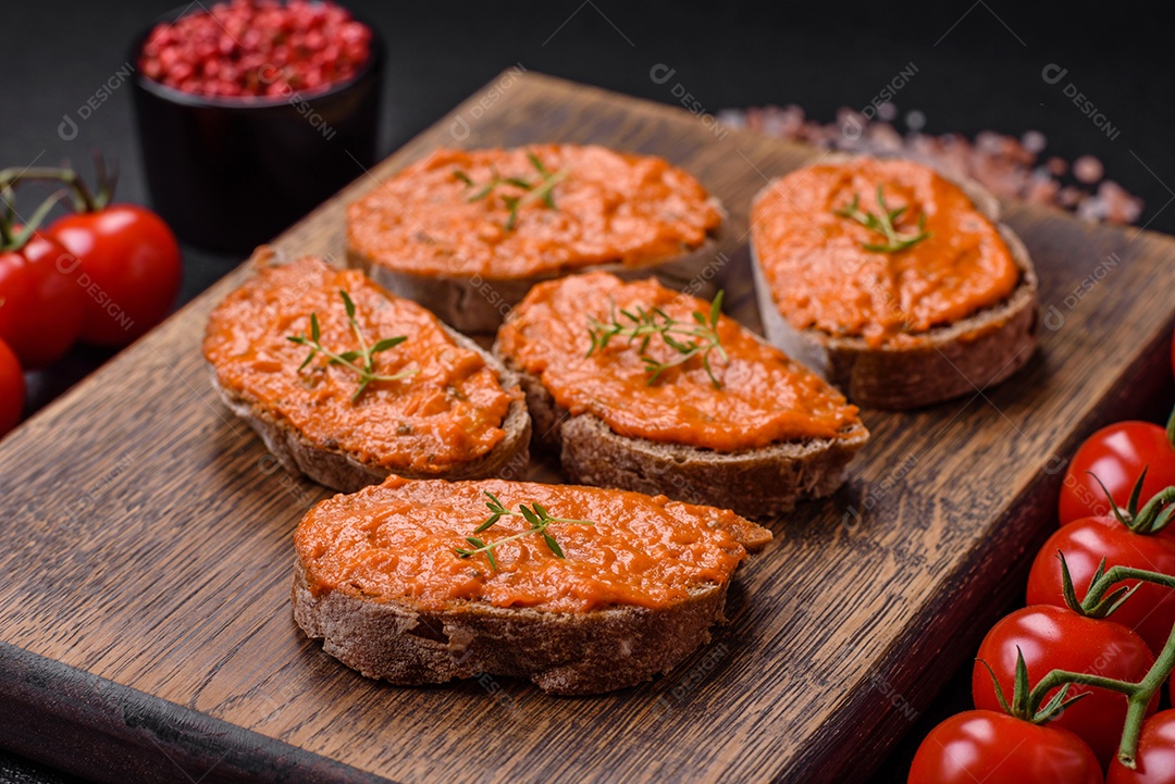 Delicioso sanduíche composto por torradas, molho vermelho com sal, especiarias e ervas sobre um fundo escuro de concreto