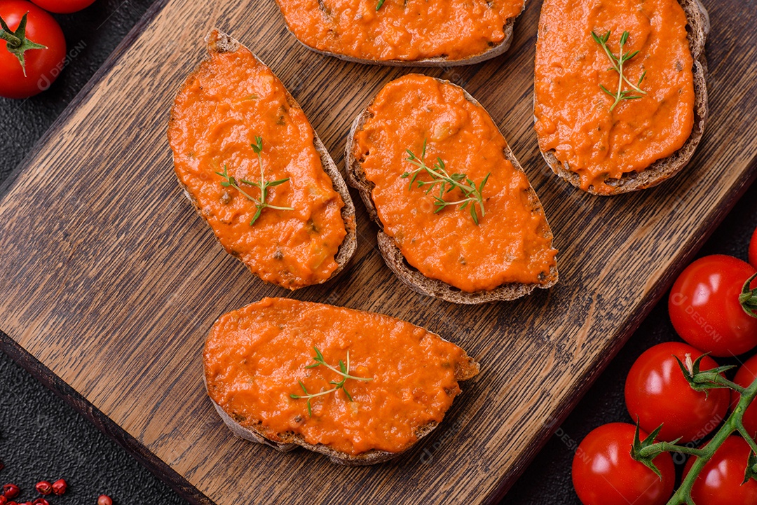 Delicioso sanduíche composto por torradas, molho vermelho com sal, especiarias e ervas sobre um fundo escuro de concreto