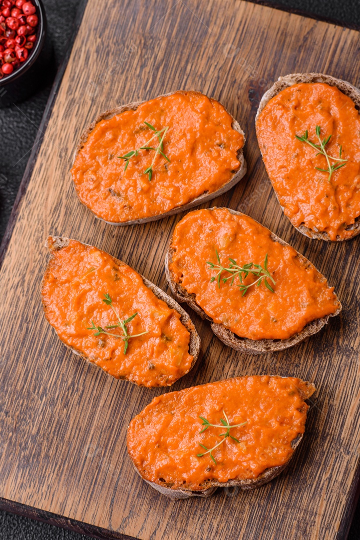 Delicioso sanduíche composto por torradas, molho vermelho com sal, especiarias e ervas sobre um fundo escuro de concreto