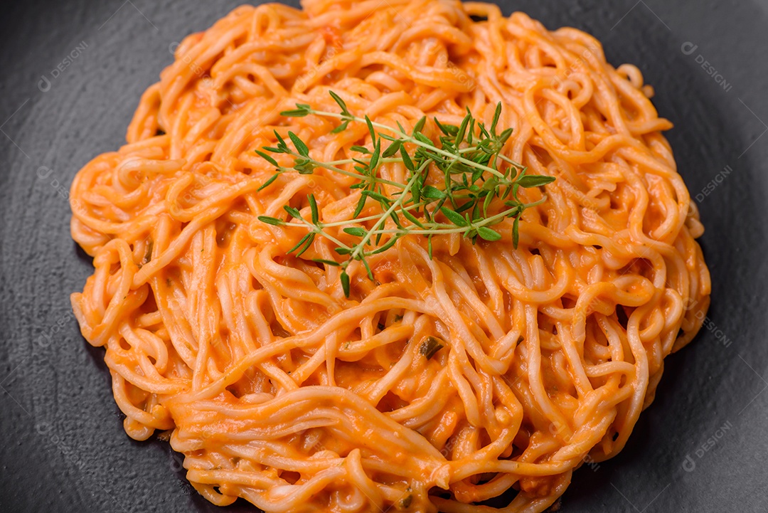 Deliciosa massa fresca composta por macarrão fino, molho pesto rosso vermelho com sal, especiarias e ervas sobre um fundo escuro de concreto