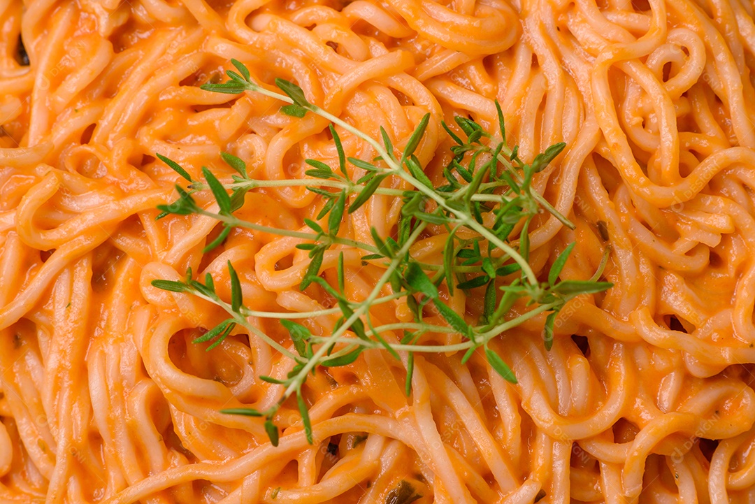 Deliciosa massa fresca composta por macarrão fino, molho pesto rosso vermelho com sal, especiarias e ervas sobre um fundo escuro de concreto