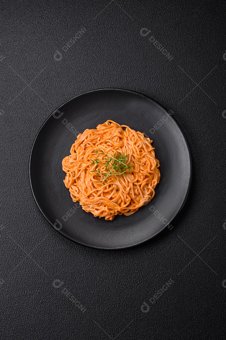 Deliciosa massa fresca composta por macarrão fino, molho pesto rosso vermelho com sal, especiarias e ervas sobre um fundo escuro de concreto