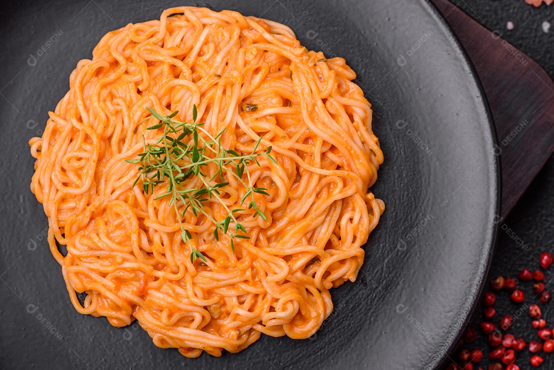 Deliciosa massa fresca composta por macarrão fino, molho pesto rosso vermelho com sal, especiarias e ervas sobre um fundo escuro de concreto