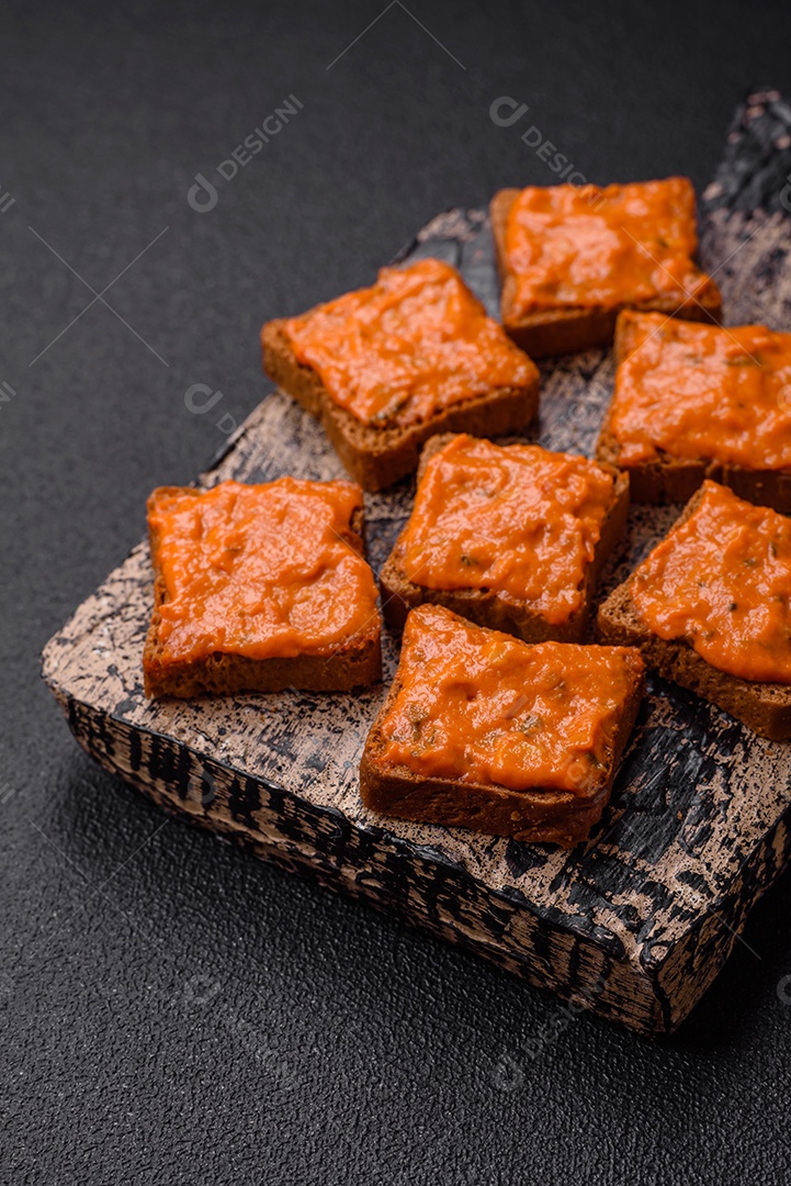 Delicioso sanduíche composto por torradas, molho vermelho com sal, especiarias e ervas sobre um fundo escuro de concreto