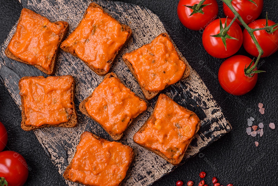 Delicioso sanduíche composto por torradas, molho vermelho com sal, especiarias e ervas sobre um fundo escuro de concreto