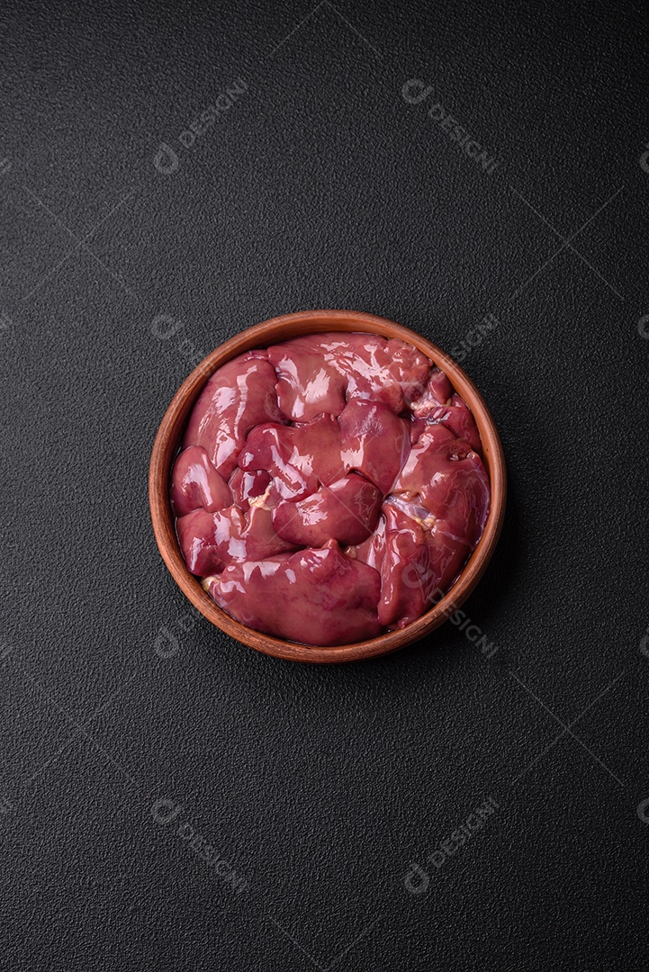 Frango cru fresco ou fígado de peru em uma placa cerâmica com sal, especiarias e ervas sobre um fundo escuro de concreto