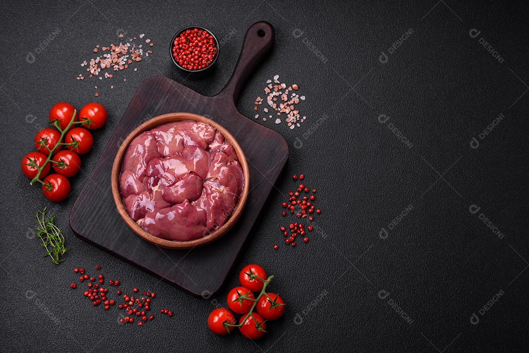 Frango cru fresco ou fígado de peru em uma placa cerâmica com sal, especiarias e ervas sobre um fundo escuro de concreto