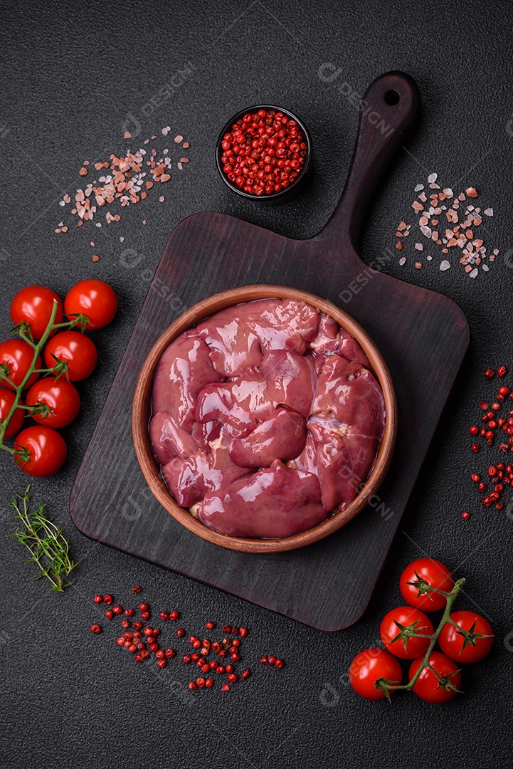 Frango cru fresco ou fígado de peru em uma placa cerâmica com sal, especiarias e ervas sobre um fundo escuro de concreto