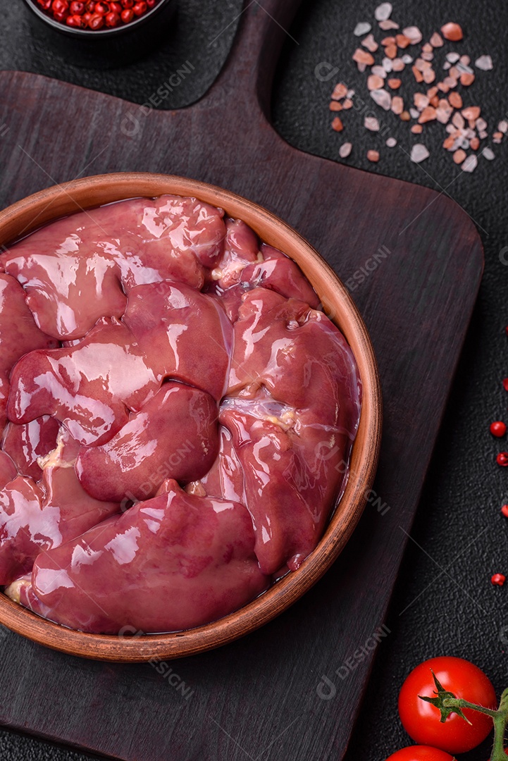 Frango cru fresco ou fígado de peru em uma placa cerâmica com sal, especiarias e ervas sobre um fundo escuro de concreto