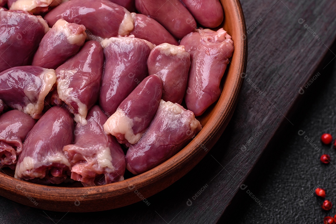 Corações frescos de frango ou peru crus em uma placa cerâmica com sal, especiarias e ervas sobre um fundo escuro de concreto