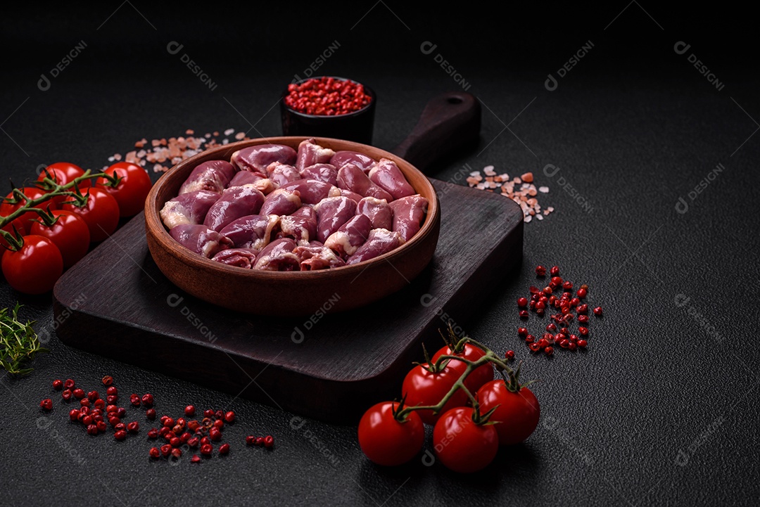 Corações frescos de frango ou peru crus em uma placa cerâmica com sal, especiarias e ervas sobre um fundo escuro de concreto