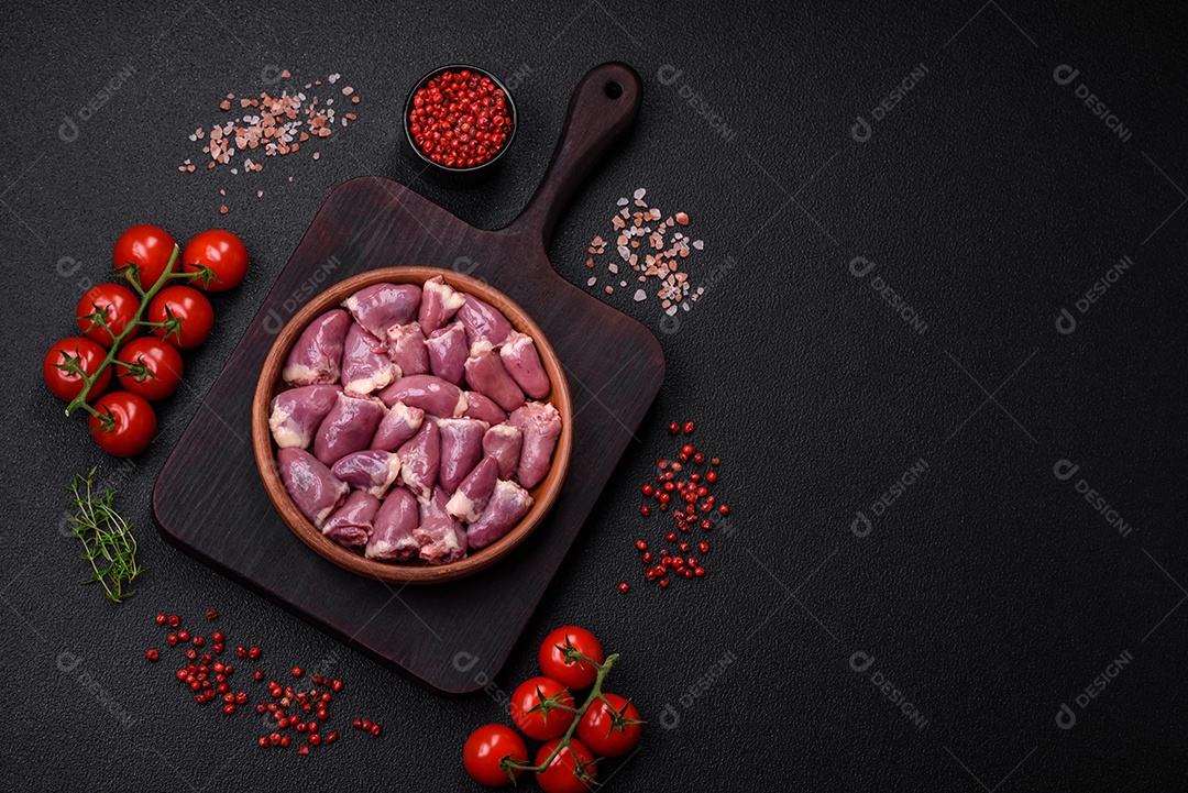 Corações frescos de frango ou peru crus em uma placa cerâmica com sal, especiarias e ervas sobre um fundo escuro de concreto