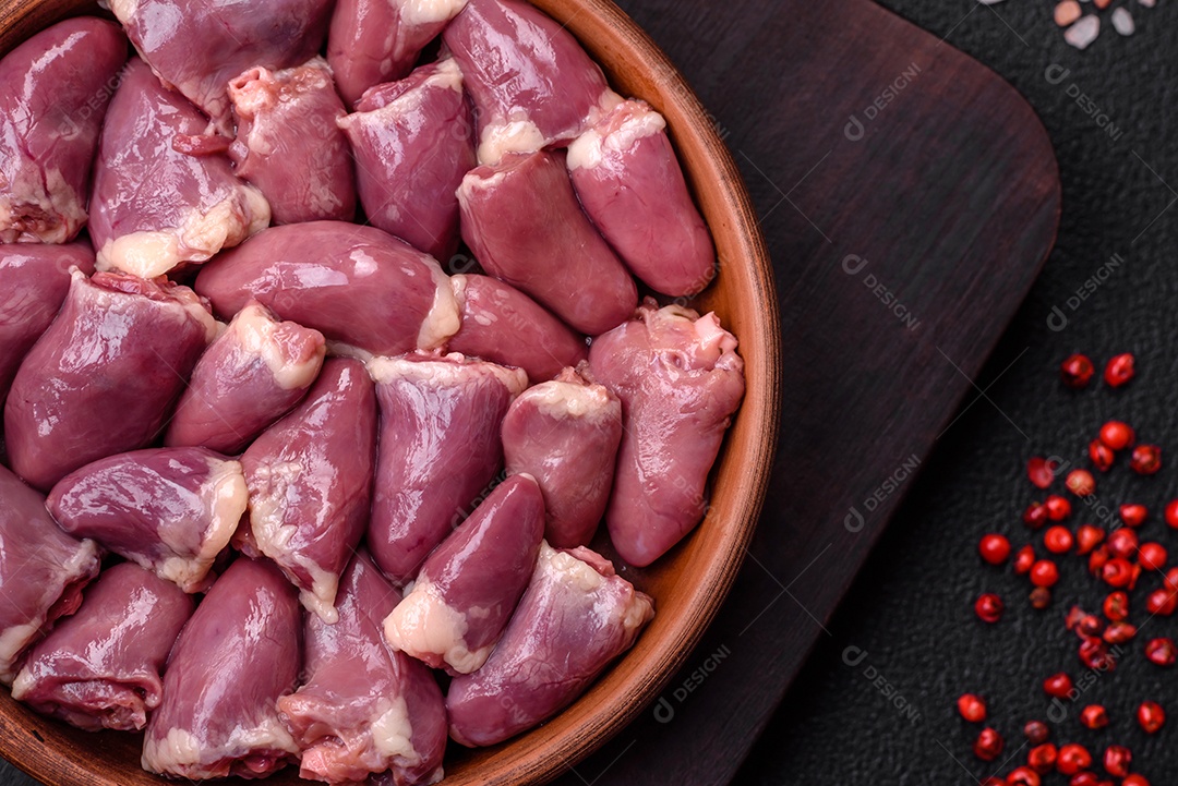 Corações frescos de frango ou peru crus em uma placa cerâmica com sal, especiarias e ervas sobre um fundo escuro de concreto