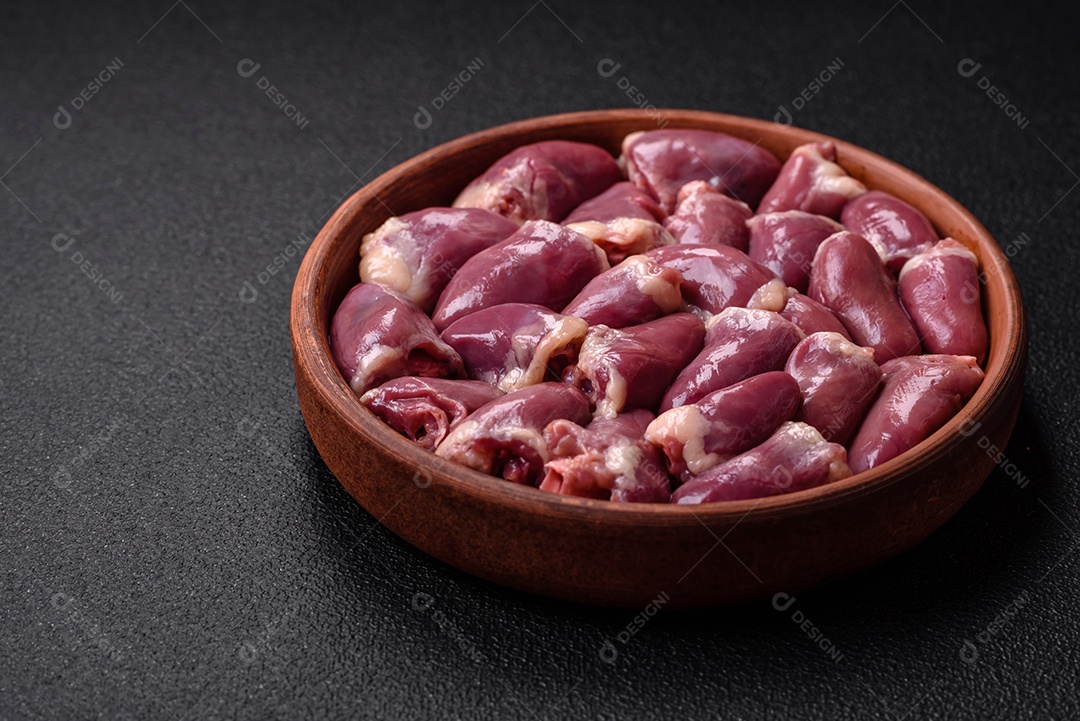 Corações frescos de frango ou peru crus em uma placa cerâmica com sal, especiarias e ervas sobre um fundo escuro de concreto