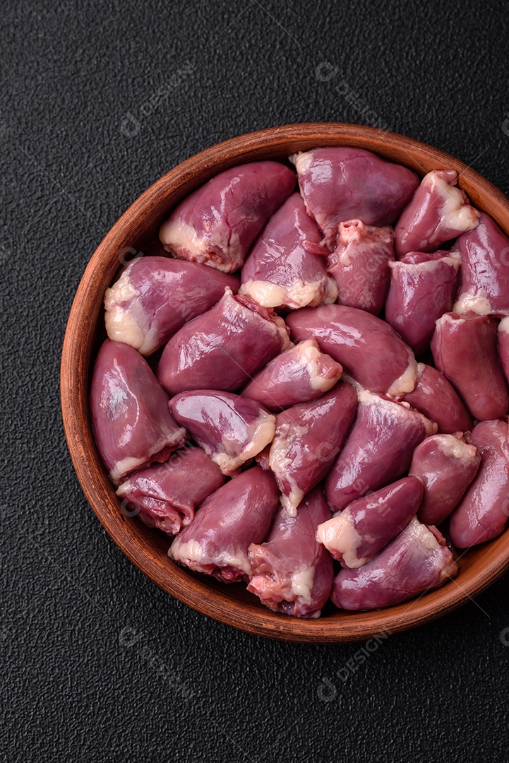 Corações frescos de frango ou peru crus em uma placa cerâmica com sal, especiarias e ervas sobre um fundo escuro de concreto