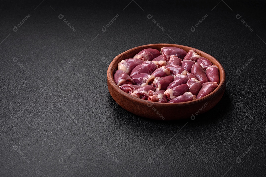 Corações frescos de frango ou peru crus em uma placa cerâmica com sal, especiarias e ervas sobre um fundo escuro de concreto