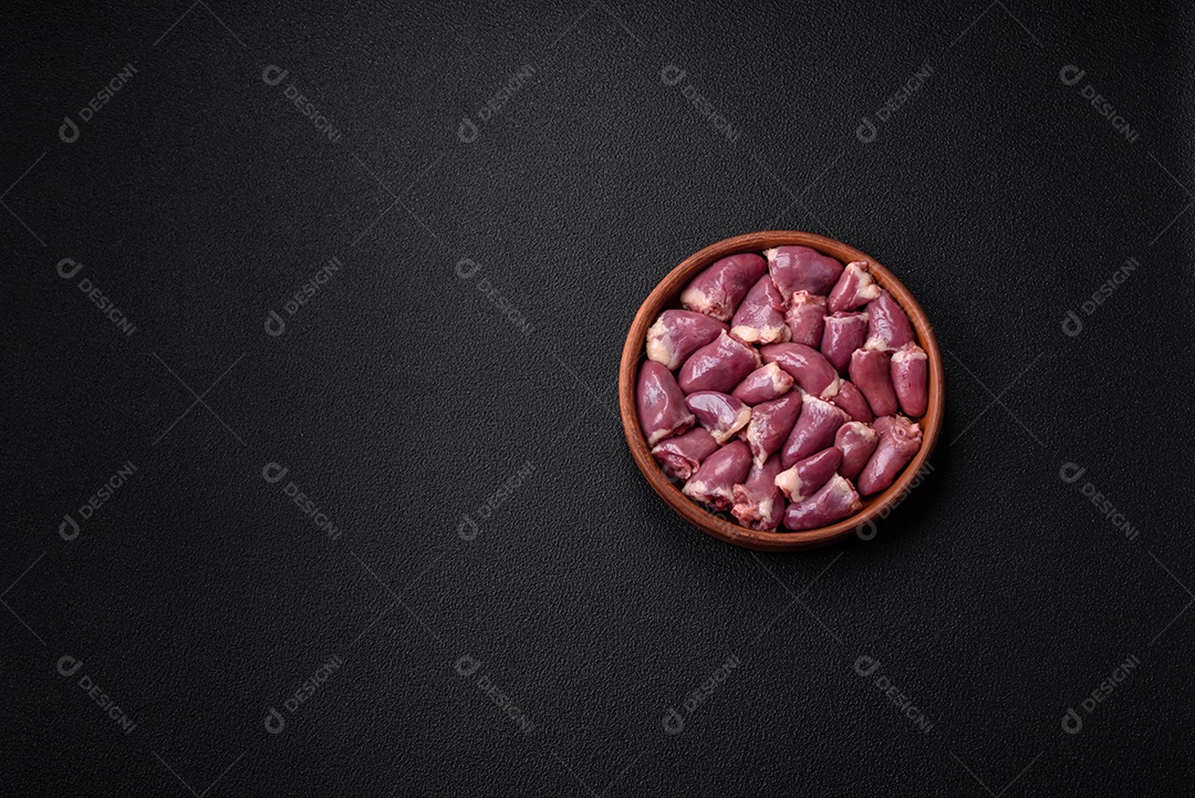 Corações frescos de frango ou peru crus em uma placa cerâmica com sal, especiarias e ervas sobre um fundo escuro de concreto