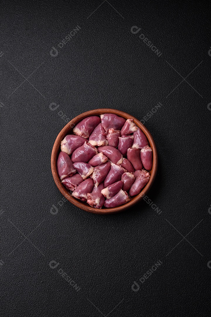 Corações frescos de frango ou peru crus em uma placa cerâmica com sal, especiarias e ervas sobre um fundo escuro de concreto