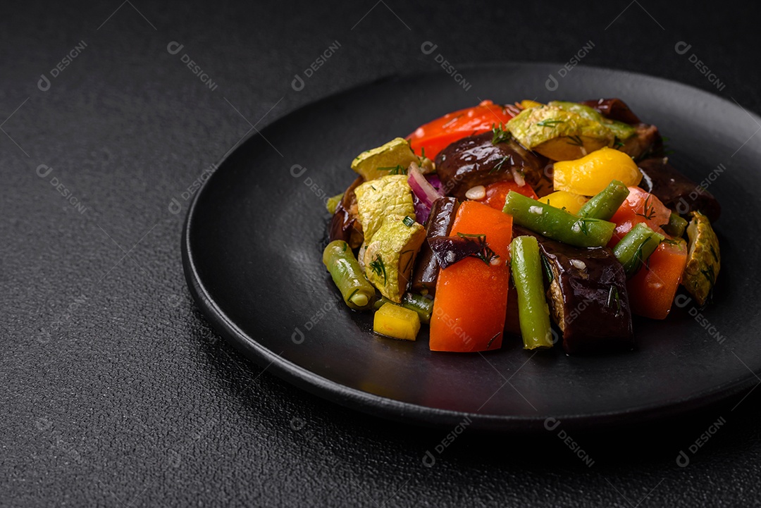 Deliciosa salada fresca e suculenta de berinjela assada, tomate, abobrinha, cebola, especiarias e sal sobre um fundo escuro de concreto