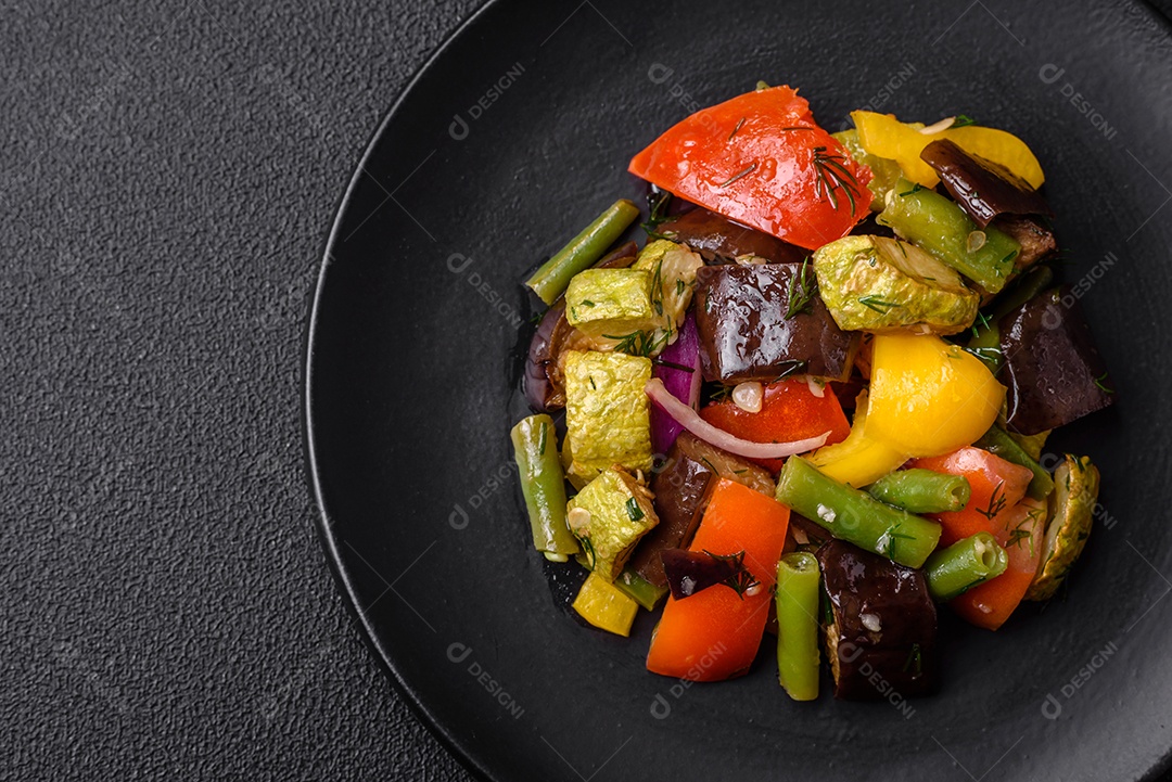 Deliciosa salada fresca e suculenta de berinjela assada, tomate, pimentão, sementes de gergelim, especiarias e sal sobre um fundo escuro de concreto