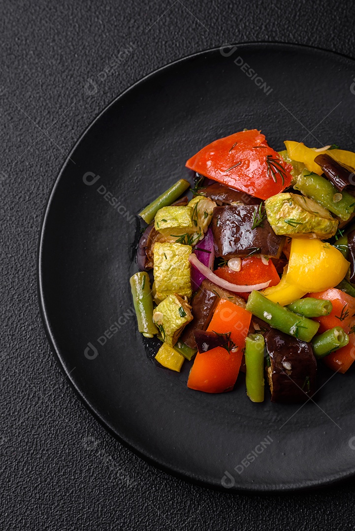 Deliciosa salada fresca e suculenta de berinjela assada, tomate, abobrinha, cebola, especiarias e sal sobre um fundo escuro de concreto