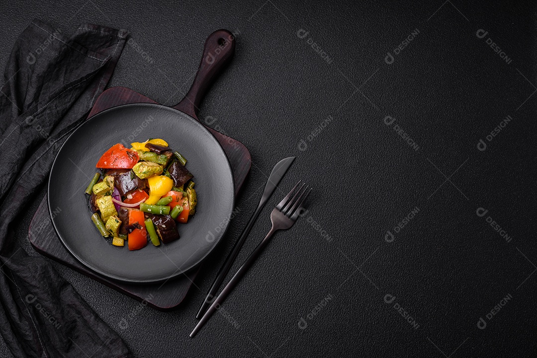 Deliciosa salada fresca e suculenta de berinjela assada, tomate, abobrinha, cebola, especiarias e sal sobre um fundo escuro de concreto