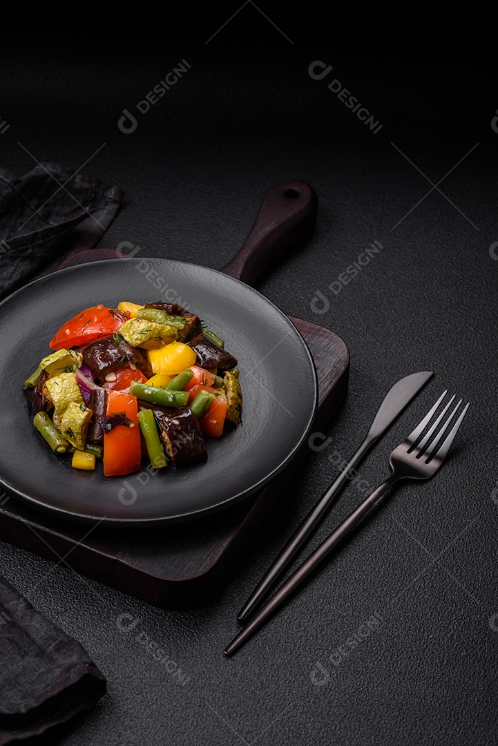 Deliciosa salada fresca e suculenta de berinjela assada, tomate, abobrinha, cebola, especiarias e sal sobre um fundo escuro de concreto